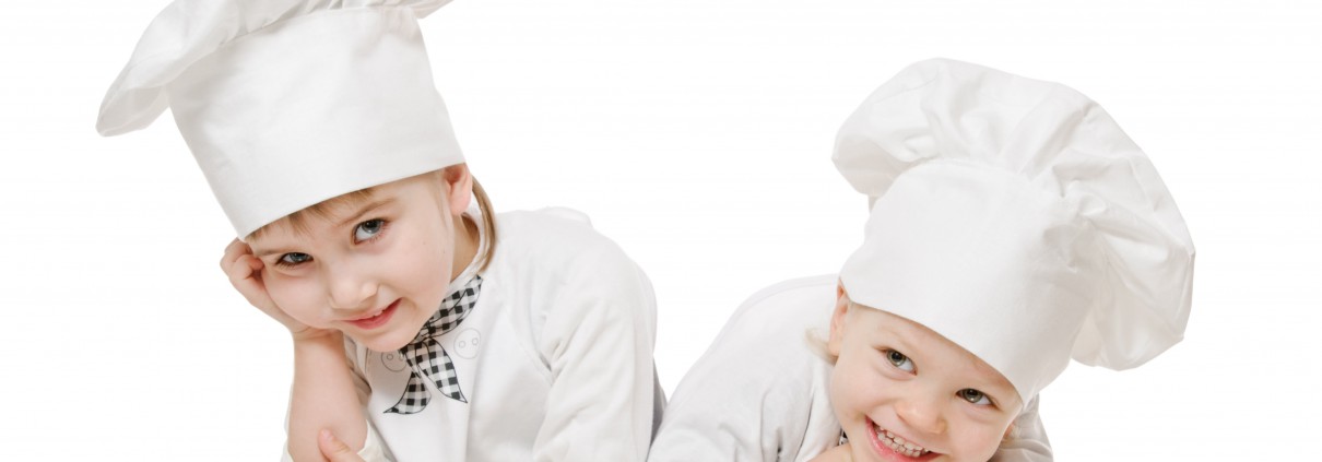 Zwei Kinder in weißen Kleidern mit Kochmützen strahlen Begeisterung für das Kochen