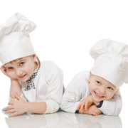 Zwei Kinder in weißen Kleidern mit Kochmützen strahlen Begeisterung für das Kochen