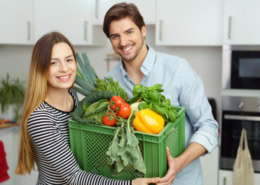 Ein junger Mann und eine junge Frau zu, die mit einem Lächeln eine volle Kiste mit frischem Gemüse tragen.