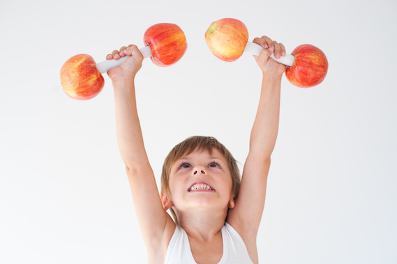Ein strahlender Junge im Alter von sieben Jahren lächelt voller Freude, während er stolz Apfelgewichte in seinen Händen hält. bio kinderverpflegung
