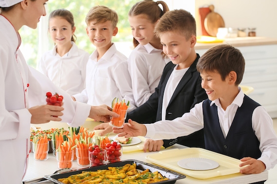 Bild von fröhlichen Schulkinder, die ein gesundes Mittagessen in der Schule essen. Bio Kinderverpflegung.