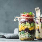 Gesunde Mahlzeit im Glas aus frischem Salat, Quinoa und Obststücken.