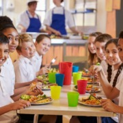 Schulcatering: Kinder sitzen am Tisch und genießen gesunde Kindermenüs.