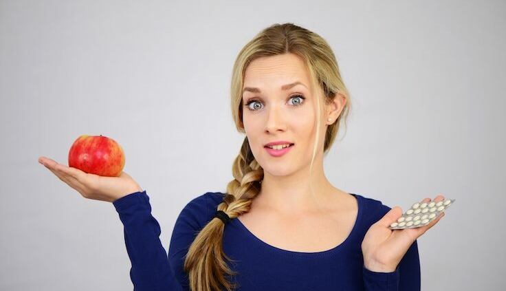 Plfanzliche Ernährung. Junge Frau hat einen Apfel auf ihrer Handfläche und hält in der anderen Hand Tabletten.