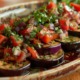 Marinierte Auberginenscheiben mit frischem Tomaten-Kräutersalat, garniert mit Petersilie und Koriander auf einer dekorativen Keramikschale.