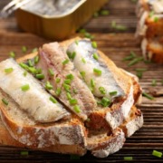 Sardinenfilets auf frischem Vollkornbrot, garniert mit gehacktem Schnittlauch, neben einer geöffneten Dose Sardinen serviert.