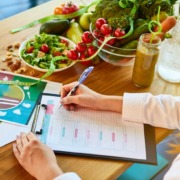 Ernährungsberaterin plant gesunde Mahlzeiten mit frischem Gemüse, Obst, Smoothies und gesunden Fetten auf dem Tisch. Die ausgewogene Ernährung wird sorgfältig nach den Prinzipien der Keto-Diät dokumentiert.