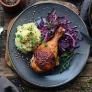 Knusprige Hähnchenkeule mit Rotkohl und Kartoffelpüree, angerichtet auf einem rustikalen Teller, begleitet von Ofenkartoffeln, mit frischen Kräutern garniert.