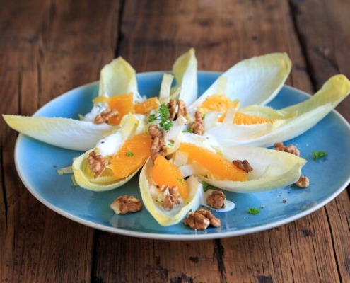 Salat aus Chicorée mit Orangenstücken, Walnüssen und frischem Dressing auf einem blauen Teller, angerichtet auf einem rustikalen Holztisch