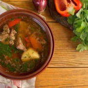 Hausgemachte Suppe mit frischem Gemüse, Kartoffeln und Rindfleisch, garniert mit gehackter Petersilie, serviert in einer braunen Schüssel auf einem rustikalen Holztisch.