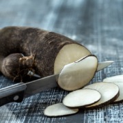 Schwarzwurzel(Schwarzer Rettich), in Scheiben geschnitten, mit einem Messer auf einem rustikalen Holztisch.