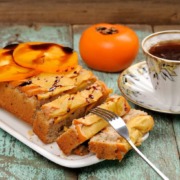 Saftiger Kuchen mit Kaki-Früchten, serviert auf einem weißen Teller mit einer Tasse Tee auf einem rustikalen Holztisch.