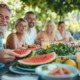 Gruppe von Menschen sitzt an einem sommerlich gedeckten Tisch im Freien und genießt leichte, erfrischende Speisen wie Wassermelone, Salat und Zitronengetränke im Schatten
