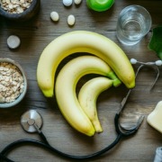 Reife Bananen mit Haferflocken, Vitamintabletten, Stethoskop und Wasserglas auf einem Holztisch – Symbolbild für gesunde Ernährung und Nährstoffe.