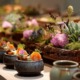 Elegantes Fingerfood in kleinen Keramikschälchen, kunstvoll garniert mit frischen Kräutern, Gemüse und Blüten – dekoriert auf einer Tafel mit Moos, Sukkulenten und floralen Elementen für ein stilvolles Event-Catering.