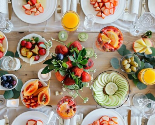Gesundes Catering-Buffet mit einer Vielzahl bunter Früchte, Smoothies, Fruchtsäften und stilvoll angerichteten Tellern – dekorativ präsentiert auf einem hellen Holztisch mit frischen Erdbeeren, Kiwis, Papayas, Beeren, Äpfeln und exotischen Obstsorten.