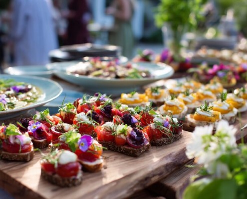 Rustikales Buffet mit gesunden, bunt angerichteten Häppchen auf Holzplatten, serviert im Freien mit Blumendeko im Hintergrund