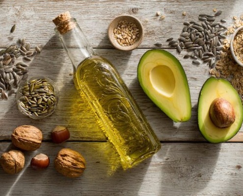 Avocadohälfte, Walnüsse und eine Flasche Öl auf Holz – gesunde Fette für den Stoffwechsel