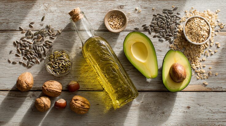 Avocadohälfte, Walnüsse und eine Flasche Öl auf Holz – gesunde Fette für den Stoffwechsel