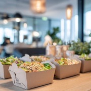 Nachhaltige Catering-Lunchboxen gefüllt mit frischen, bunten Bowls aus Gemüse, Hülsenfrüchten und Körnern, serviert in moderner Büro-Atmosphäre.
