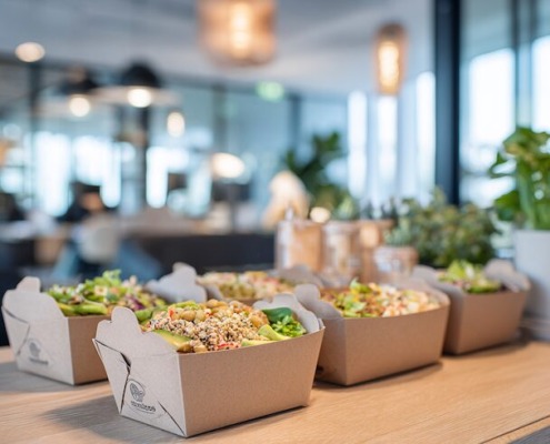 Nachhaltige Catering-Lunchboxen gefüllt mit frischen, bunten Bowls aus Gemüse, Hülsenfrüchten und Körnern, serviert in moderner Büro-Atmosphäre.