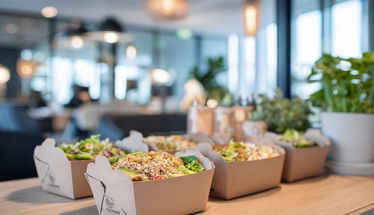Nachhaltige Catering-Lunchboxen gefüllt mit frischen, bunten Bowls aus Gemüse, Hülsenfrüchten und Körnern, serviert in moderner Büro-Atmosphäre.