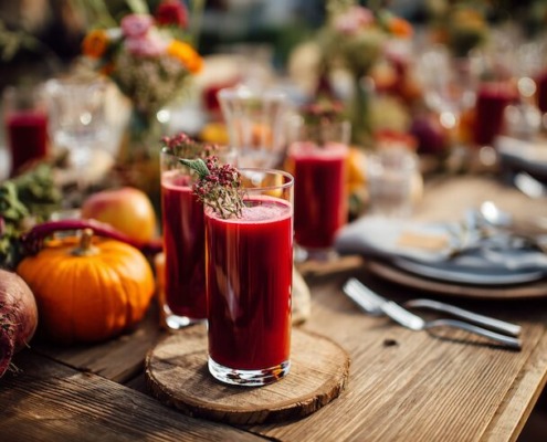 Catering-Tisch mit Mehrweg-Gläsern gefüllt mit Rote-Bete-Saft, saisonales Herbstgemüse (Kürbis, Rote Bete, Äpfel) als Dekoration, moderne Bio-Catering-Atmosphäre, natürliche Holztische, frische Farben, freundliche Stimmung, perfekt für Event oder Kindergarten-Catering