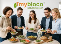 Nachhaltiges Catering von mybioco in einem modernen, hellen Büro – liebevoll angerichtetes Buffet mit regionalen und saisonalen Bio-Speisen, frischen Salaten und knusprigem Brot. Junge Menschen im modernen Casual-Office-Look genießen gemeinsam das Essen in entspannter, freundlicher Atmosphäre. Das mybioco-Logo steht für Genuss mit Verantwortung und echte Nachhaltigkeit.