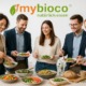 Nachhaltiges Catering von mybioco in einem modernen, hellen Büro – liebevoll angerichtetes Buffet mit regionalen und saisonalen Bio-Speisen, frischen Salaten und knusprigem Brot. Junge Menschen im modernen Casual-Office-Look genießen gemeinsam das Essen in entspannter, freundlicher Atmosphäre. Das mybioco-Logo steht für Genuss mit Verantwortung und echte Nachhaltigkeit.