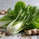 Frisch angerichteter Pak Choi auf einem hellen Holztisch, mit glänzenden grünen Blättern und weißen Stielen, daneben frischer Ingwer, Knoblauch und Sesamsamen, natürliches Licht, modernes Food-Styling, asiatisches Flair
