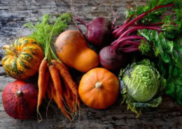Wunderschön arrangiertes Ensemble aus orangefarbenem Gemüse (Karotten, Hokkaido-Kürbis, roter Paprika, Feldsalat) neben grünen Blattgemüsen (Spinat, Grünkohl); starker Farbkontrast, natürliches Gegenlicht, hochwertige Food-Fotografie