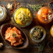 ernährung nach antibiotika Wunderschön arrangiertes Flatlay probiotischer Lebensmittel: Joghurt, Kefir, Sauerkraut, Kimchi, eingelegtes Gemüse, rustikaler Holzuntergrund, weiches natürliches Licht, hochwertige Food-Fotografie, sehr detailreich.