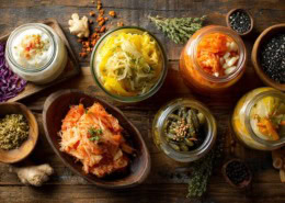 Wunderschön arrangiertes Flatlay probiotischer Lebensmittel: Joghurt, Kefir, Sauerkraut, Kimchi, eingelegtes Gemüse, rustikaler Holzuntergrund, weiches natürliches Licht, hochwertige Food-Fotografie, sehr detailreich.