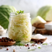 Sauerkraut gesund Schön arrangiertes Glas mit fermentiertem Sauerkraut, umgeben von Weißkohl, Salz und Gewürzen; sauberes, helles natürliches Licht, minimalistischer Wellness-Stil, probiotisches Lebensmittel.