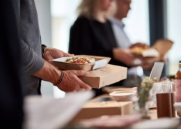 Verpflegung im Unternehmen ohne Kantine, moderne Büroumgebung, Mitarbeitende sitzen gemeinsam an einem Tisch, Lunch-Bowls und warme Mahlzeiten, natürlich angerichtet, ruhige, professionelle Stimmung, Tageslicht, keine Kantine sichtbar, authentischer Arbeitsalltag