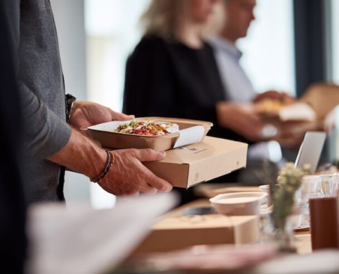 Verpflegung im Unternehmen ohne Kantine, moderne Büroumgebung, Mitarbeitende sitzen gemeinsam an einem Tisch, Lunch-Bowls und warme Mahlzeiten, natürlich angerichtet, ruhige, professionelle Stimmung, Tageslicht, keine Kantine sichtbar, authentischer Arbeitsalltag