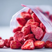 Offene, nachhaltige Verpackung mit zerkleinerten getrockneten Erdbeeren, fast wie Pulver, , natürliche unperfekte Stücke sichtbar, klare und gut lesbare Inhaltsstoffliste auf der Verpackung, cleanes modernes Design, sanfte natürliche Lichtstimmung, ehrliche Produktdarstellung ohne Inszenierung
