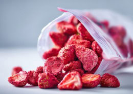 Offene, nachhaltige Verpackung mit zerkleinerten getrockneten Erdbeeren, fast wie Pulver, , natürliche unperfekte Stücke sichtbar, klare und gut lesbare Inhaltsstoffliste auf der Verpackung, cleanes modernes Design, sanfte natürliche Lichtstimmung, ehrliche Produktdarstellung ohne Inszenierung