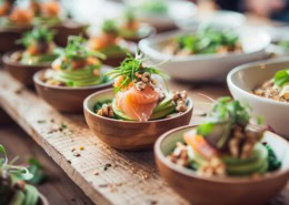 Brainfood Business Lunch Catering mit kleinen Schalen, Lachs, Avocado, Nüssen und frischem Gemüse, modern angerichtet auf Holztisch im Bio-Stil