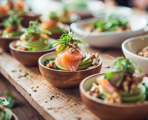 Brainfood Business Lunch Catering mit kleinen Schalen, Lachs, Avocado, Nüssen und frischem Gemüse, modern angerichtet auf Holztisch im Bio-Stil